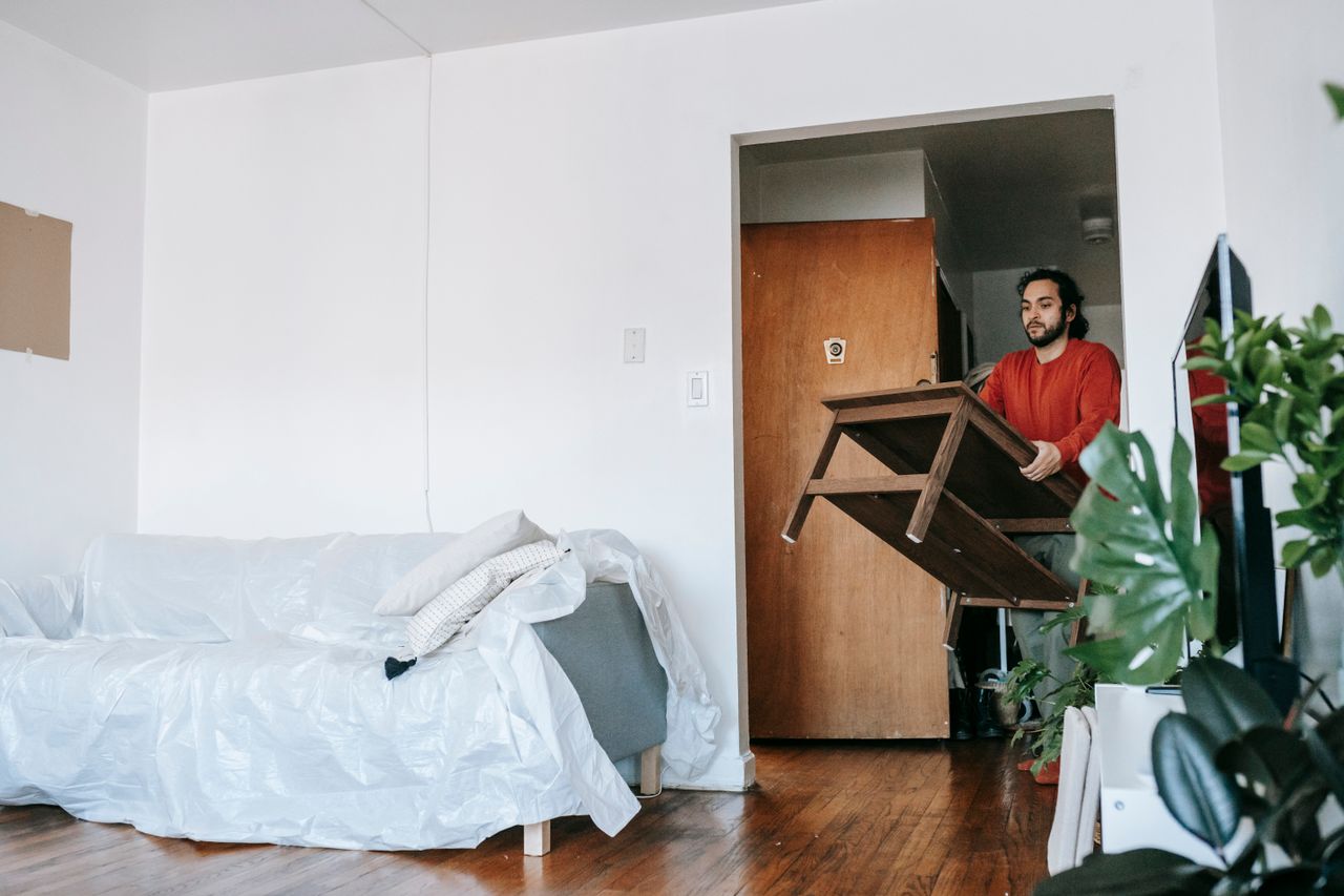 Homme tenant une table en bois pendant un déménagement dans un appartement contemporain.